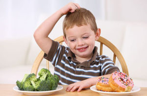 Young boy making choice between broccoli and doughnuts...B6ABW8 Young boy making choice between broccoli and doughnuts